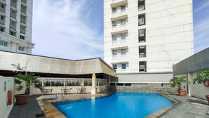 A swimming pool with a covered seating area, surrounded by potted plants and a tall building in the background. - Best Deal 3Br Apartment Braga City Walk (Bandung)