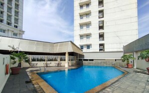 A swimming pool with a covered seating area, surrounded by potted plants and a tall building in the background. - Best Deal 3Br Apartment Braga City Walk (Bandung)