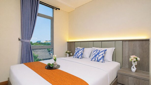 Ein Hotelzimmer mit einem Bett, einem Nachttisch, einem Fenster mit Vorhängen und Blick ins Freie.