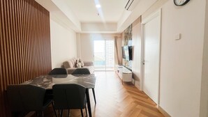 A modern living space with a dining area, a sofa, a TV, and a wooden floor. - Great Value 2Br At Apartment Podomoro City Deli Medan (Medan)