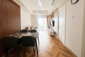 A modern living space with a dining area, a sofa, a TV, and a wooden floor. - Great Value 2Br At Apartment Podomoro City Deli Medan (Medan)