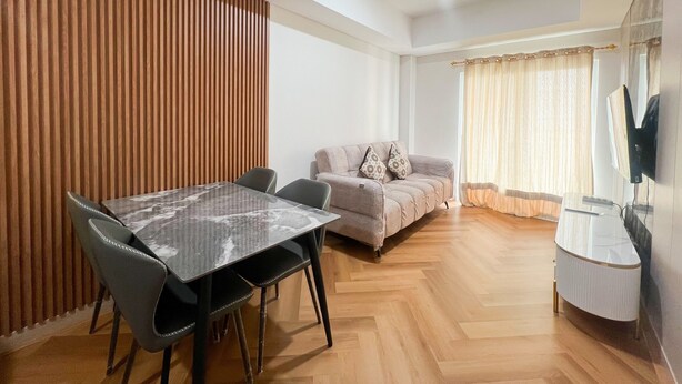 A modern living room with a dining table, sofa, and a flat-screen TV mounted on the wall. - Great Value 2Br At Apartment Podomoro City Deli Medan (Medan)