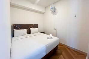 A neatly made bed with white linens, a headboard with a geometric design, and a wall-mounted fan. - Great Value 2Br At Apartment Podomoro City Deli Medan (Medan)