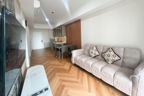A modern living room with a sofa, a small dining table, and a kitchen area in the background. - Great Value 2Br At Apartment Podomoro City Deli Medan (Medan)