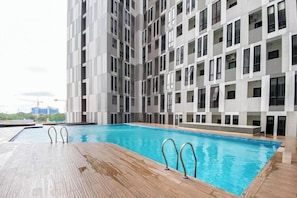A modern building with a swimming pool and a wooden deck. - Nice Look Studio Apartment at The Alton (Semarang)