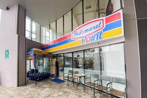 Un magasin Indomaret Point doté d’une façade en verre, d’un espace extérieur avec des sièges et d’un tapis bleu menant à l’entrée.