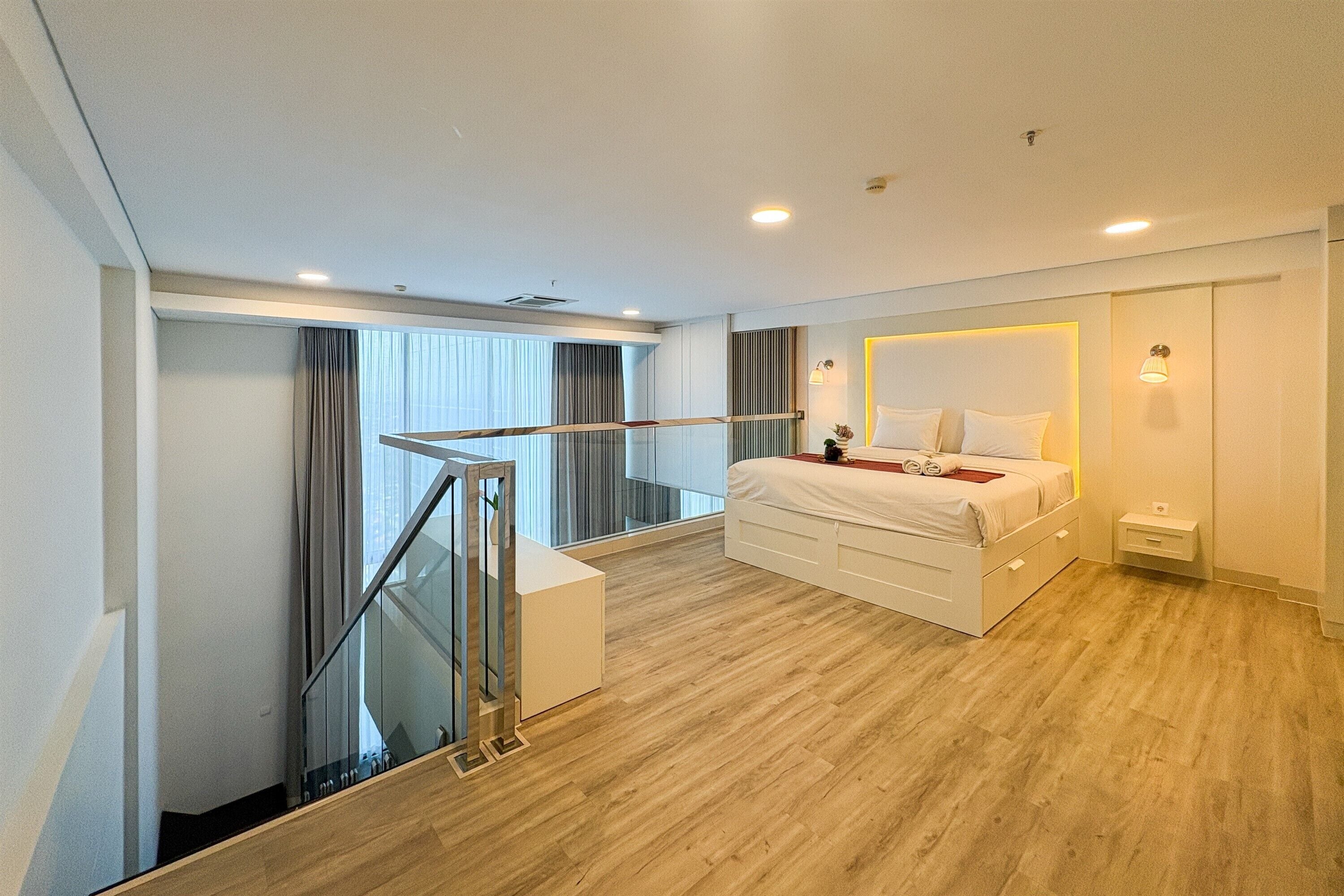 Une chambre moderne avec un grand lit, une table de chevet, une commode et un balcon doté d’une balustrade en verre.