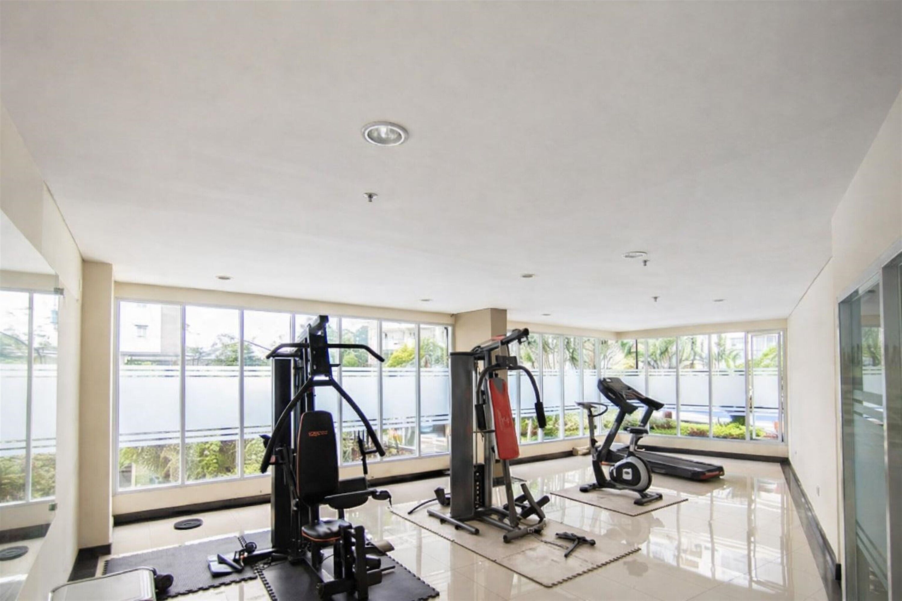 Ett gym med olika typer av träningsutrustning, stora fönster och utsikt över omgivningen.
