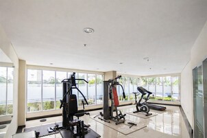 Un gimnasio con diversos equipos de ejercicio, ventanas amplias y vistas al exterior.