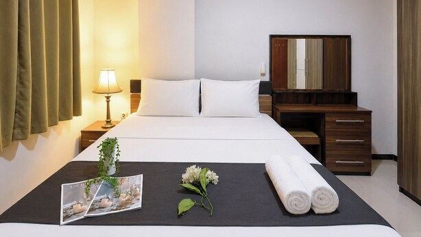 A hotel room with a bed, bedside table, lamp, mirror, and a neatly made bed with a photo frame and flowers. - Comfortable 2Br At Gateway Pasteur Apartment (Bandung)