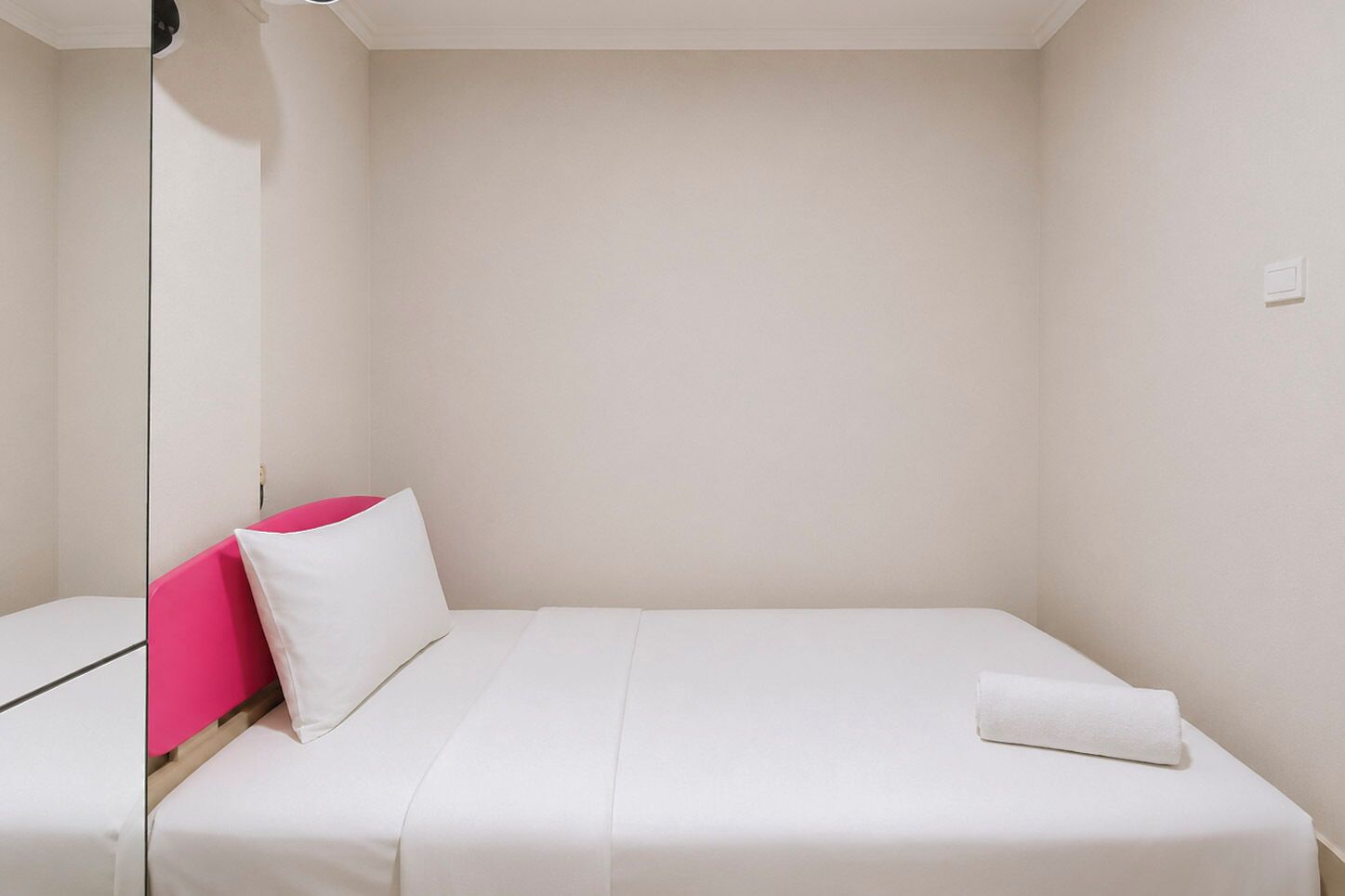 A single-bed room with a white bedspread, a white pillow, and a pink pillow.