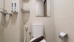 A bathroom with a toilet, a shower, a towel, a toilet paper holder, and a mirror. - Comfortable 2Br At Gateway Pasteur Apartment (Bandung)