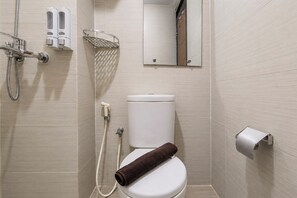 A bathroom with a toilet, a shower, a towel, a toilet paper holder, and a mirror. - Comfortable 2Br At Gateway Pasteur Apartment (Bandung)