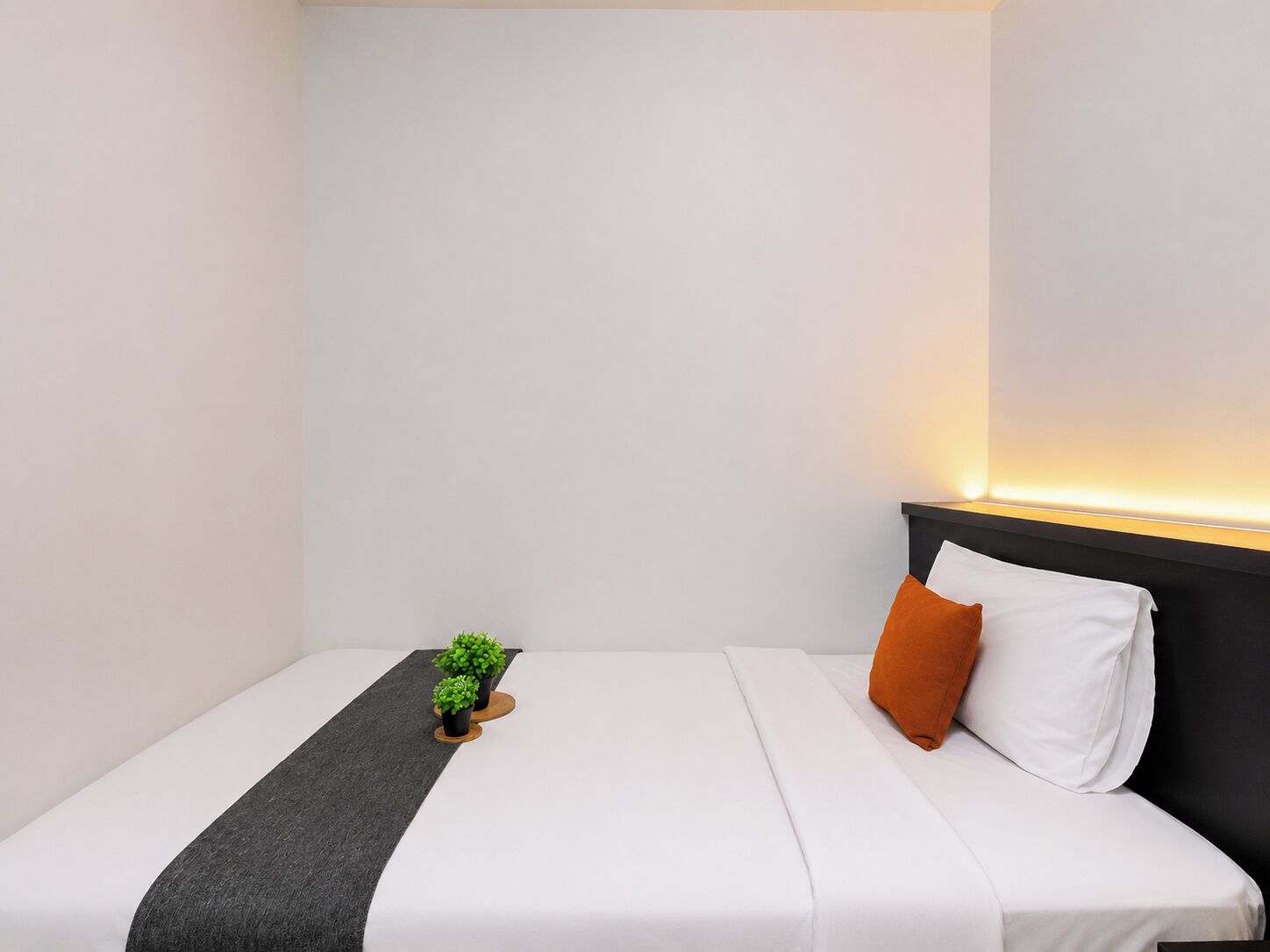 Een hotelkamer met een bed, nachtkastje, en een kleine plant in een pot.