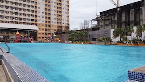 A swimming pool with a slide and play area, surrounded by a high-rise building and a construction site. - Airy And Modern 2Br At Apartment Teluk Intan (Jakarta)