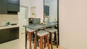 A modern kitchen with a dining area, including a refrigerator, sink, and bar stools. - Airy And Modern 2Br At Apartment Teluk Intan (Jakarta)