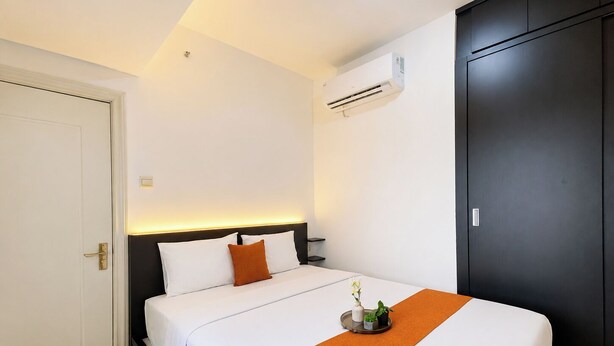 A hotel room with a bed, a bedside table, an air conditioning unit, and a wardrobe. - Airy And Modern 2Br At Apartment Teluk Intan (Jakarta)