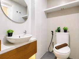 A modern bathroom with a white sink, mirror, and toilet, and two potted plants on the counter.