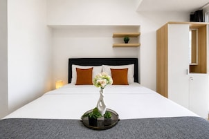 A hotel room with a bed, a bedside lamp, a small shelf with a plant, and a wardrobe.