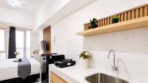 A modern hotel room with a bed, a flat-screen TV, a coffee machine, a sink, and a wooden shelf with plants. - Modern Well Located Studio Room At Apartment Tokyo Riverside Pik 2 (Jakarta)