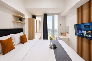A hotel room with a bed, a TV, a window with a view, and a plant on the bedside table.