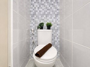 A bathroom with a toilet, a shower, and a tiled wall. - Modern Well Located Studio Room At Apartment Tokyo Riverside Pik 2 (Jakarta)