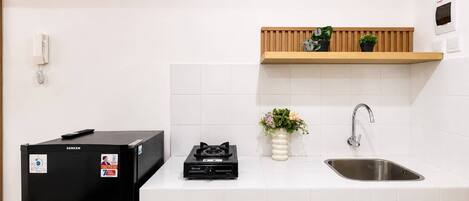 Una cocina con un refrigerador negro, una estufa a gas, un estante de madera con plantas, un salpicadero de azulejos blancos y un lavamanos de acero inoxidable.