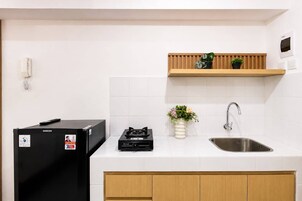 Una cocina con un refrigerador negro, una estufa a gas, un estante de madera con plantas, un salpicadero de azulejos blancos y un lavamanos de acero inoxidable.