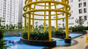 Zona de piscina exterior moderna con una fuente amarilla y abundante vegetación.