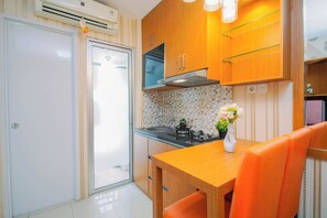A compact kitchen with a built-in stove, wooden cabinets, and a small dining area with a table and chairs. - Well Appointed 2Br At Apartment Bassura City (Jakarta)