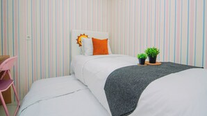 Una cama individual con cabecera blanca, un almohadón naranja y dos macetas con plantas.