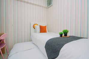 A single bed with a white headboard, an orange pillow, and two potted plants. - Well Appointed 2Br At Apartment Bassura City (Jakarta)