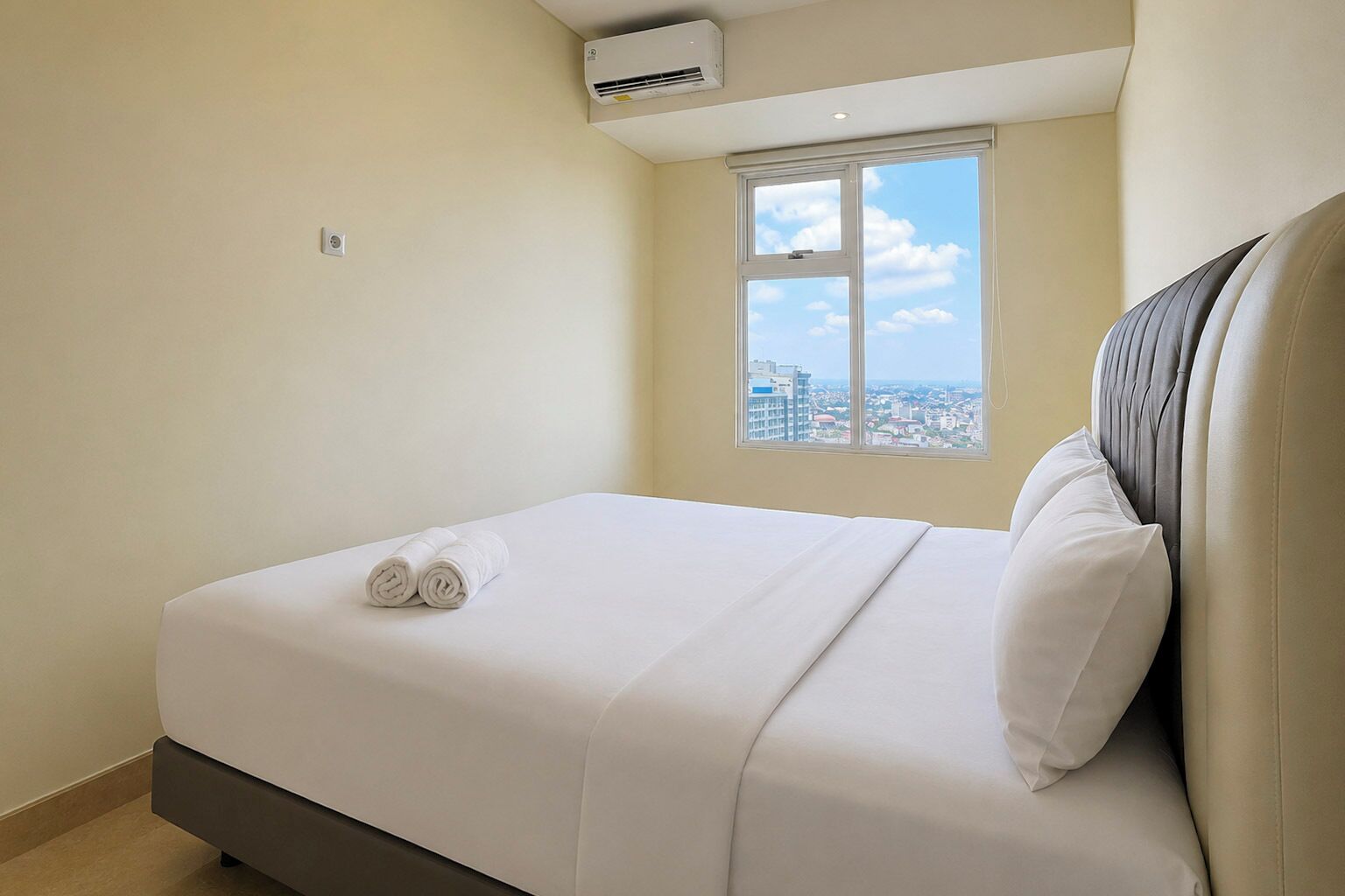 Une chambre d’hôtel avec un lit, une fenêtre donnant sur la ville et un appareil de climatisation.