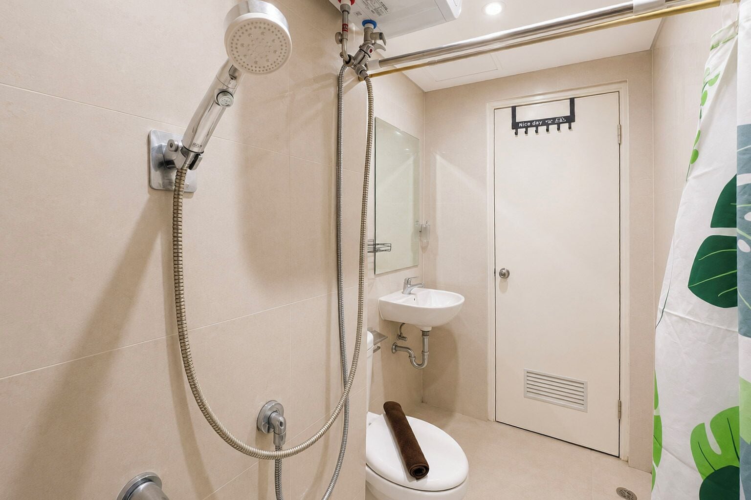 Casa de banho com chuveiro, sanita, lavatório e toalha pendurada na parede.
