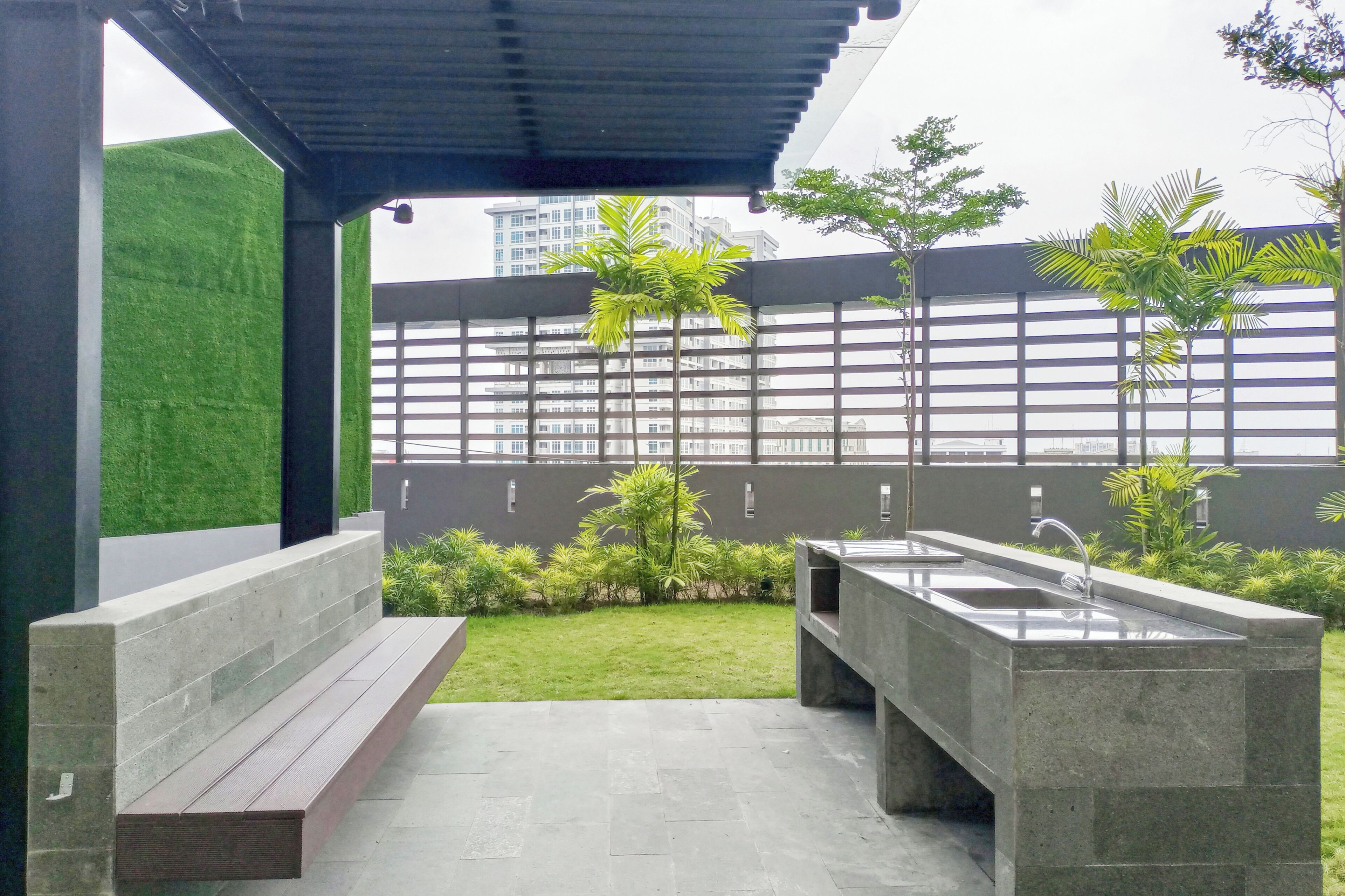 Un área exterior moderna con asientos, una banca, un lavabo y un pequeño jardín con palmeras.