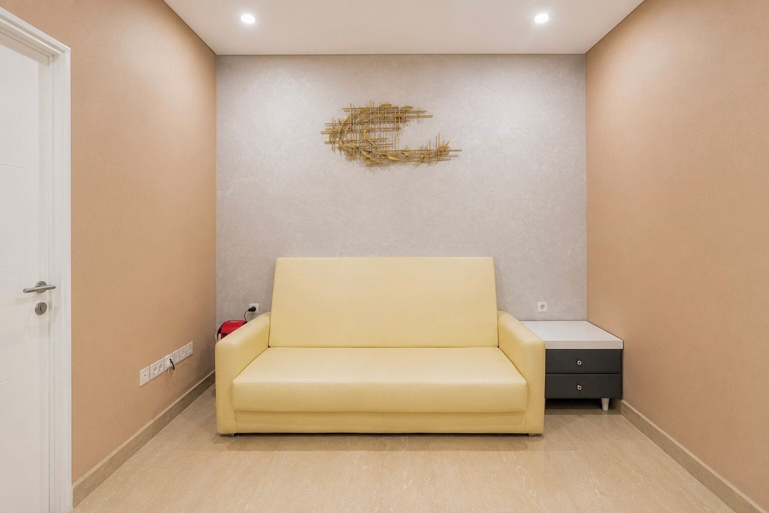 A room with a yellow sofa, a small bedside table, and a wall-mounted abstract art piece.