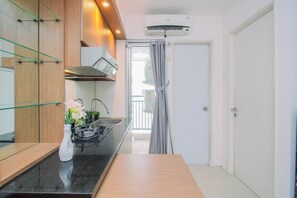 Cocina compacta con estufa a gas, lavamanos y horno integrado. Se aprecia un mueble de madera con puertas de cristal y un florero con flores sobre la encimera.