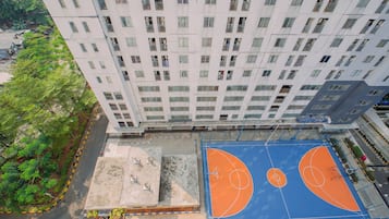 En høj bygning med flere balkoner, en basketballbane og grøn beplantning omkring.