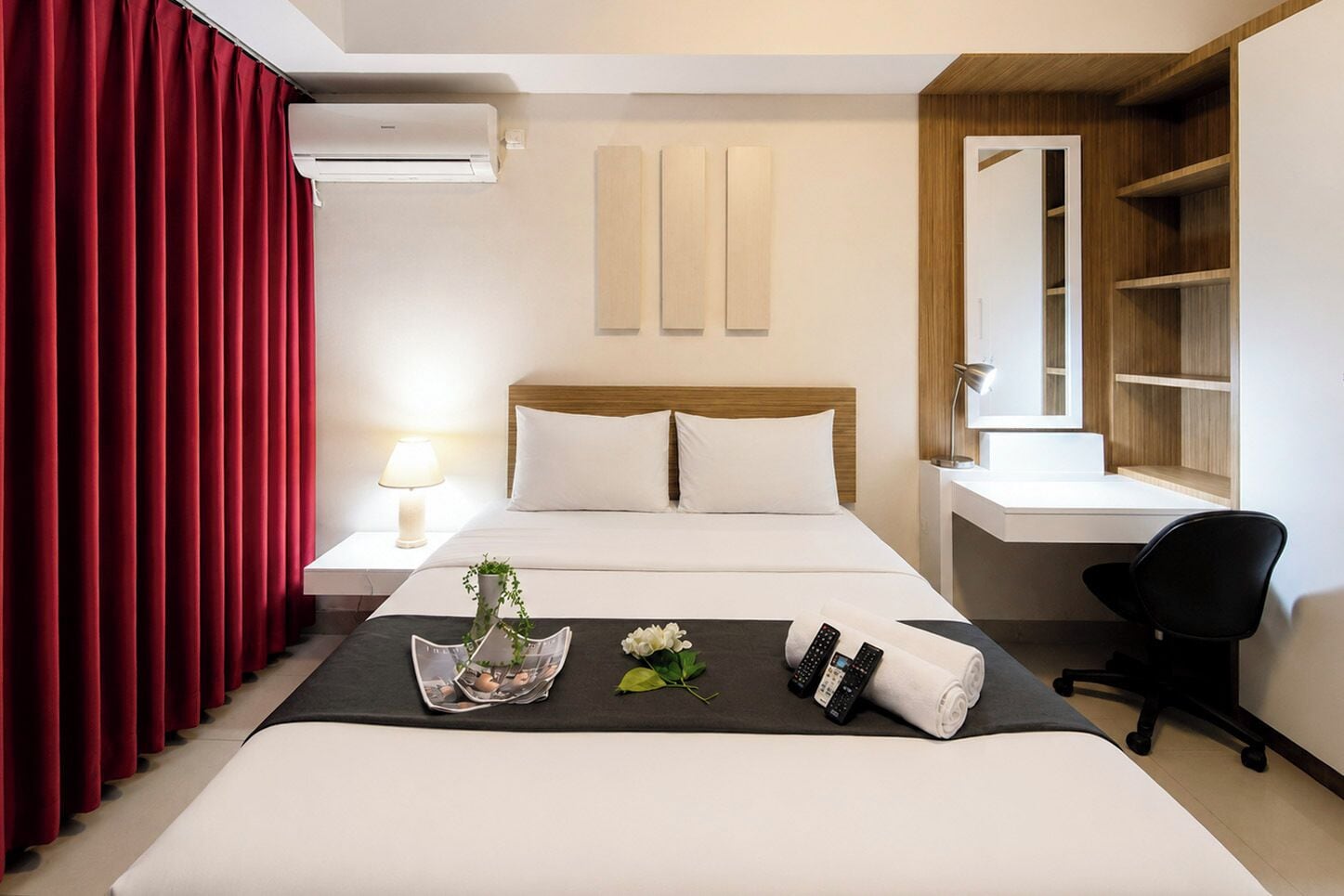 A hotel room with a bed, a desk, a chair, a lamp, and a window with a view of a building.