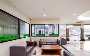 A hotel lobby with seating, a reception desk, and large windows with signage. - Nice Look Studio At Apartment Beverly Dago (Bandung)