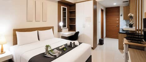 A modern hotel room with a bed, bedside table, TV, wardrobe, and kitchenette.