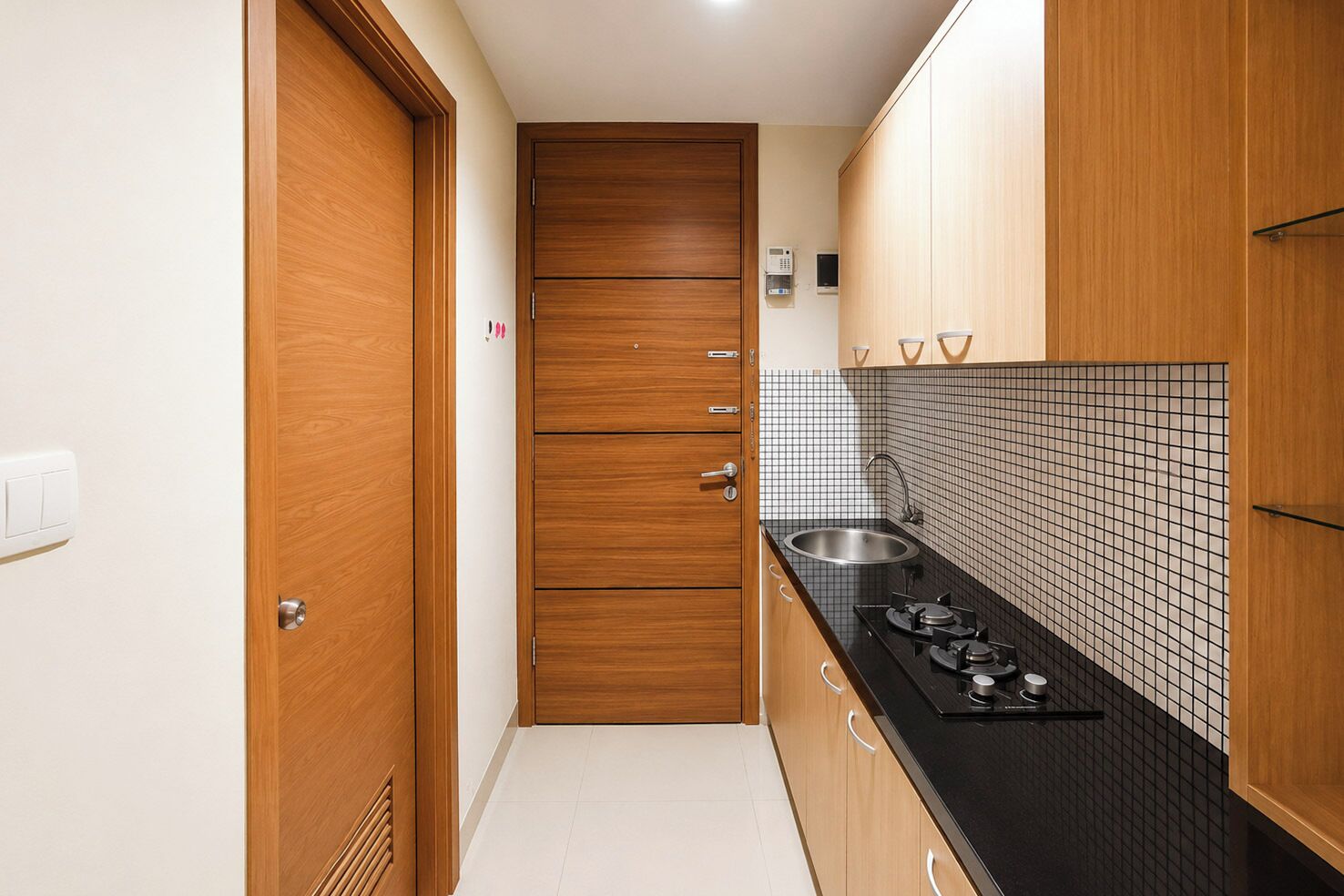 Una cocina estrecha con armarios de madera, encimera negra, pileta de acero inoxidable y salpicadero de azulejos.
