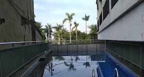 A swimming pool with a metal railing, surrounded by buildings and palm trees. - Nice Look Studio At Apartment Beverly Dago (Bandung)