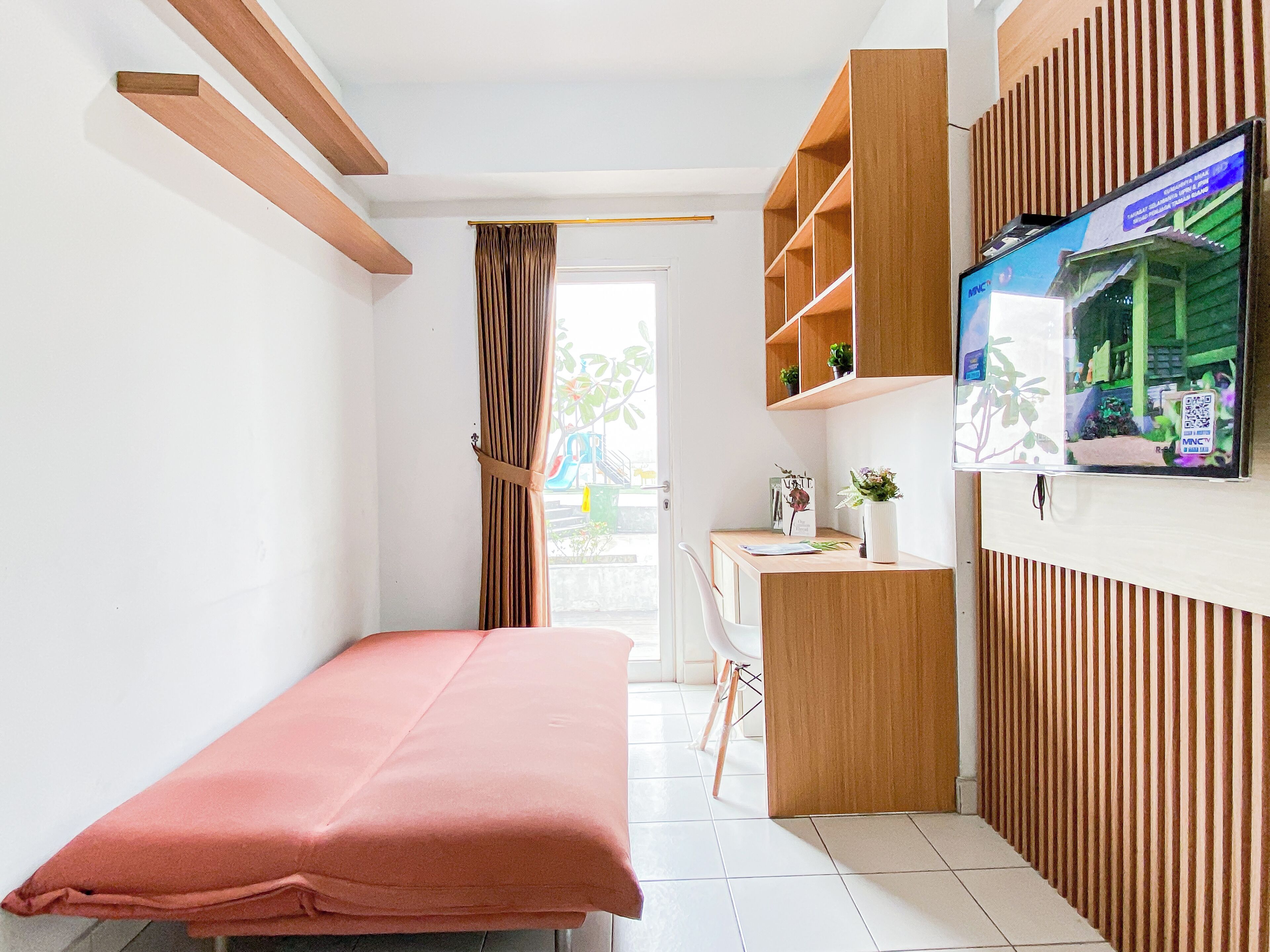 Ein Schlafzimmer mit einem Bett, einem Schreibtisch, einem Fernseher und einem Fenster mit Vorhängen.