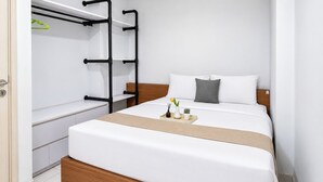 Una habitación de hotel moderna con cama, cabecero de madera, mesita de noche y estante empotrado con perchero.