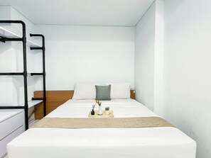 Una cama individual con cabecera de madera, ropa de cama blanca y una mesita de noche con lámpara.