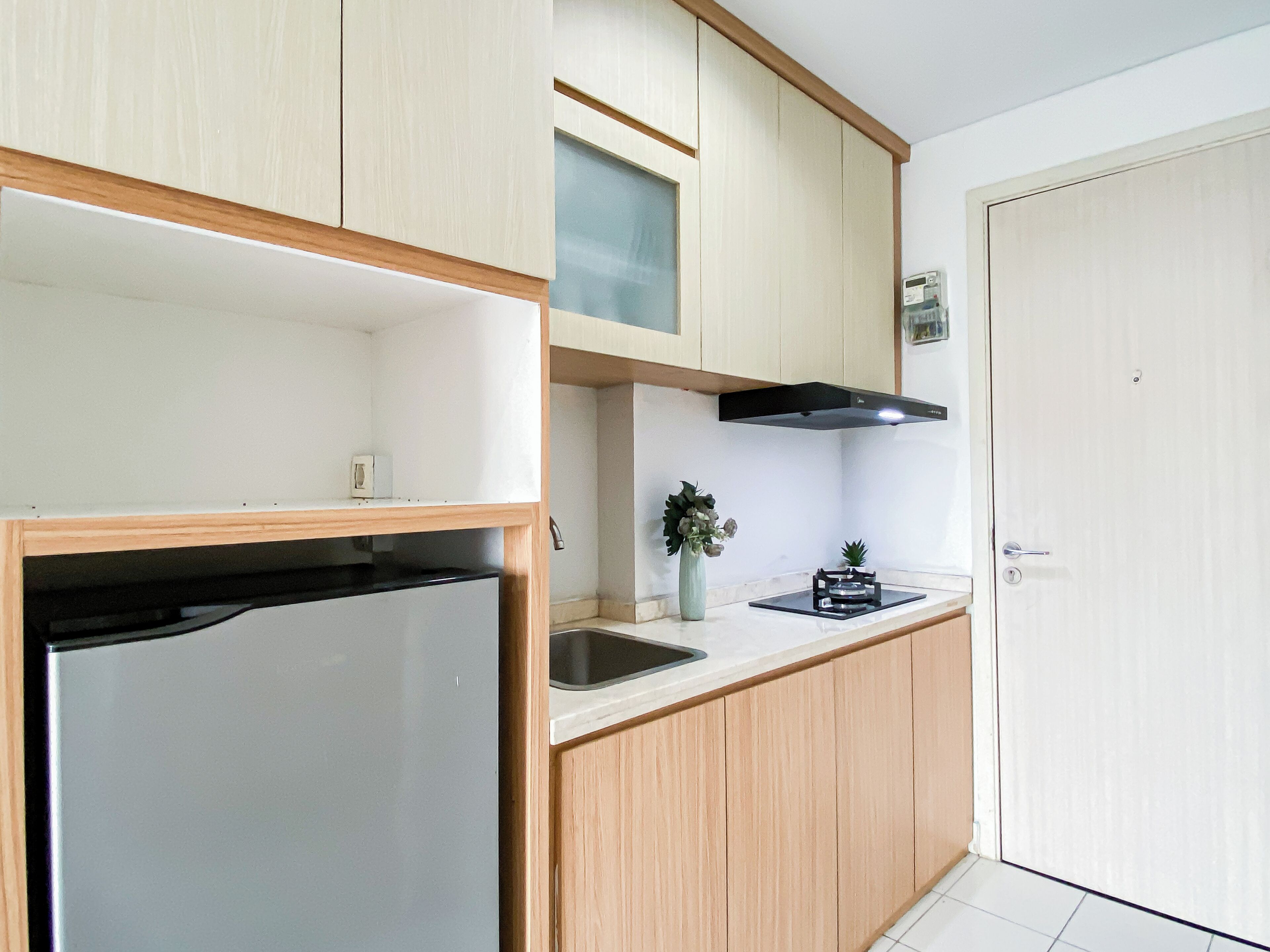 Una cocina con refrigerador, lavamanos, armarios de madera y una puerta.