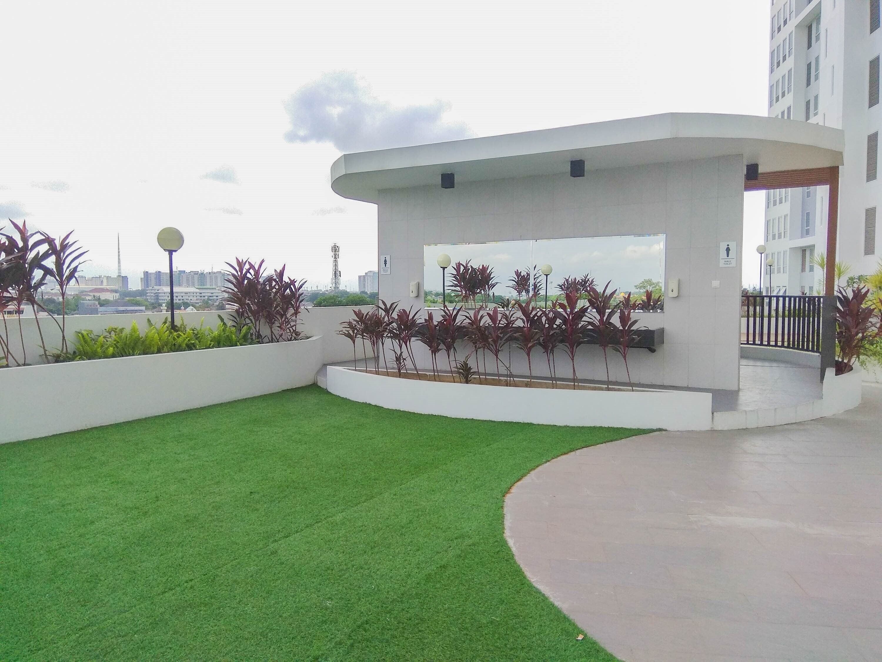 Un espacio exterior moderno con césped artificial, macetas con diversas plantas y una estructura blanca con ventana de vidrio.