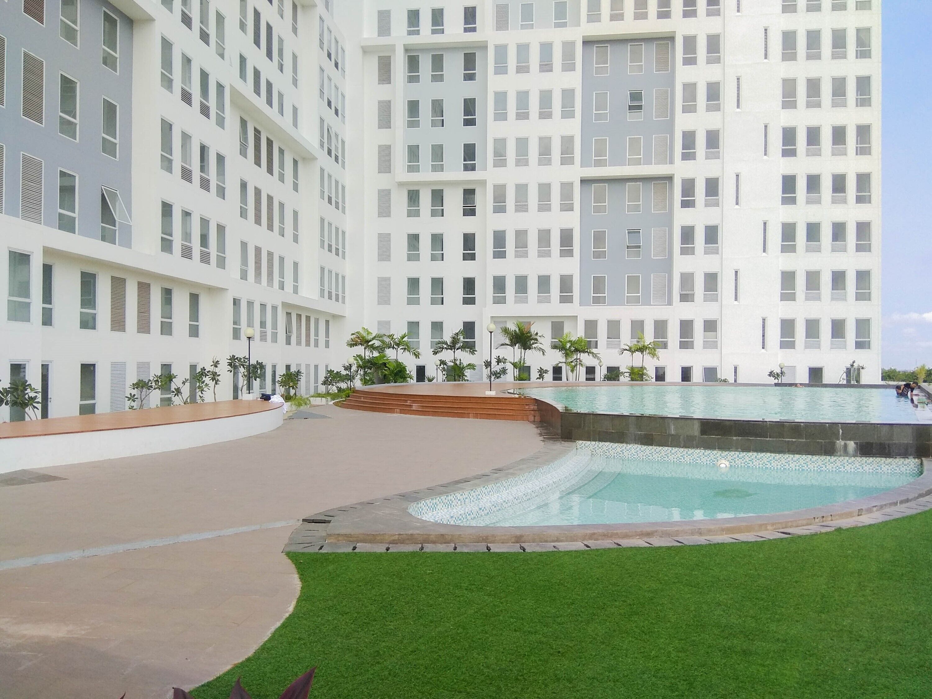 Un hotel moderno con un amplio espacio de piscina, rodeado de un césped cuidado y palmeras.