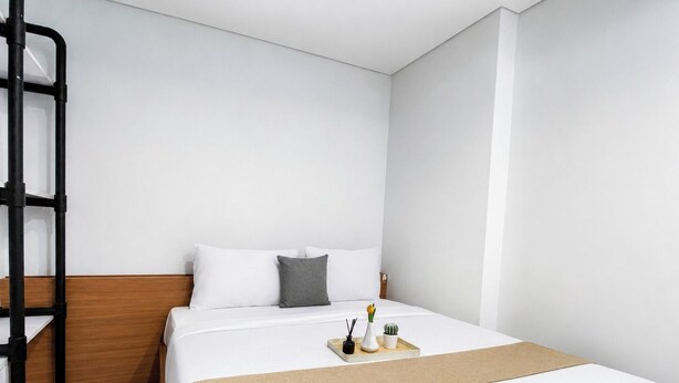 Habitación de hotel con cama, cabecera de madera, escalera de metal negro y bandeja con artículos de tocador.